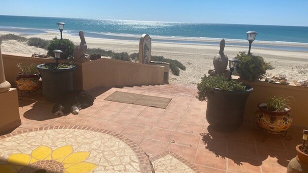 A terrace with a tiled floor, potted plants, and a view of the beach.