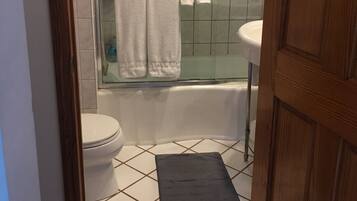 Een bad/douchecombinatie, handdoeken, zeep, toiletpapier