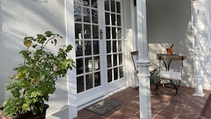A white exterior with a glass door, a potted plant, and a small table with a chair.