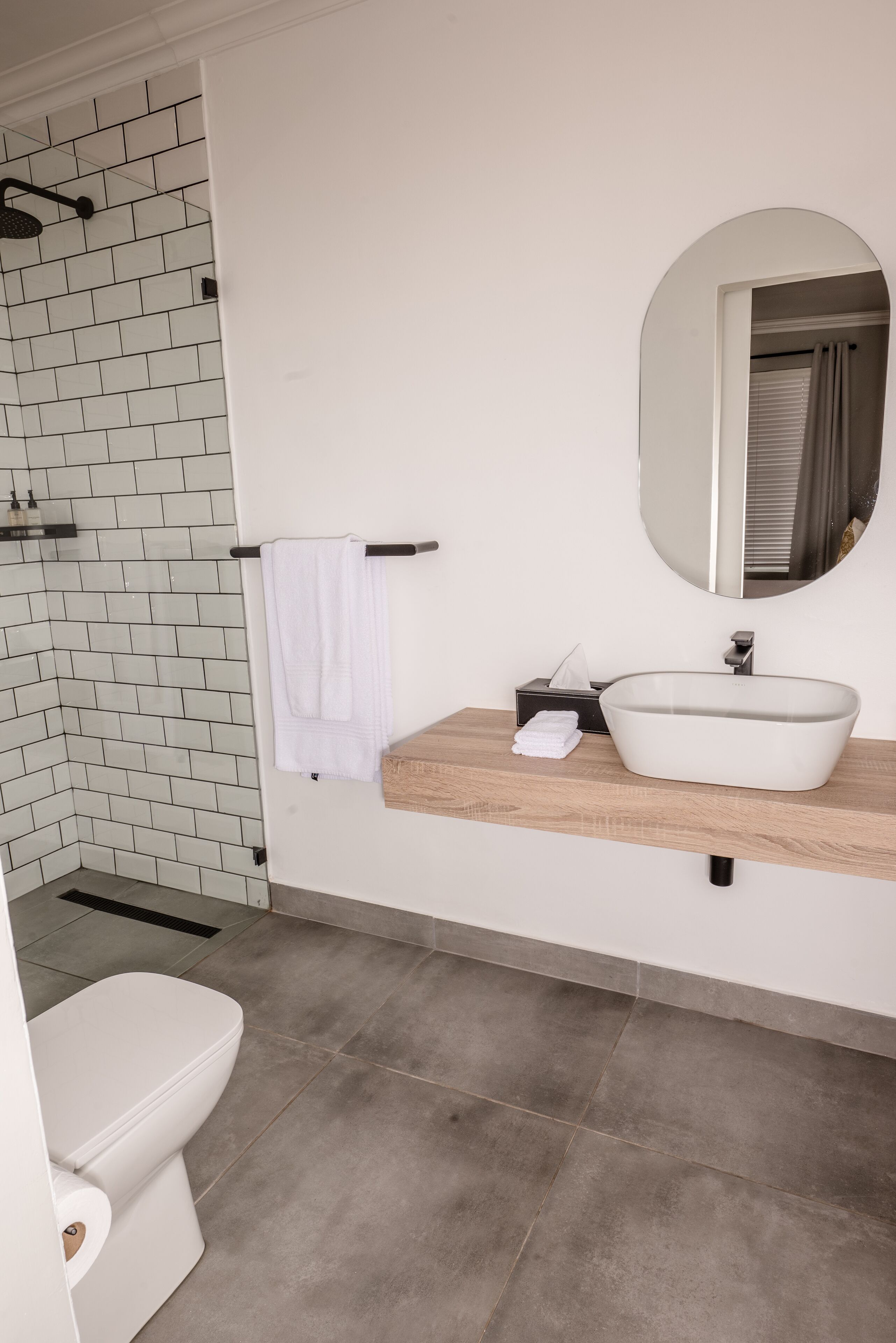 Een moderne badkamer met een witte betegelde douche, een houten wastafelmeubel met een witte wasbak en een toilet.