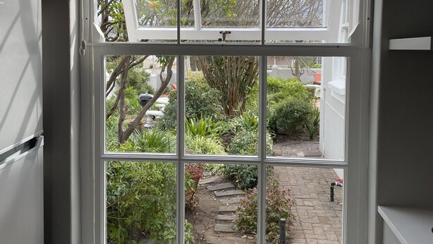A window with a view of a garden, a white wall, and a part of a white refrigerator.
