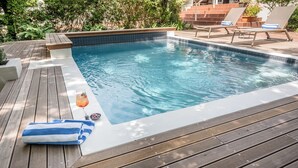 A swimming pool with a wooden deck, lounge chairs, and a drink on the side.