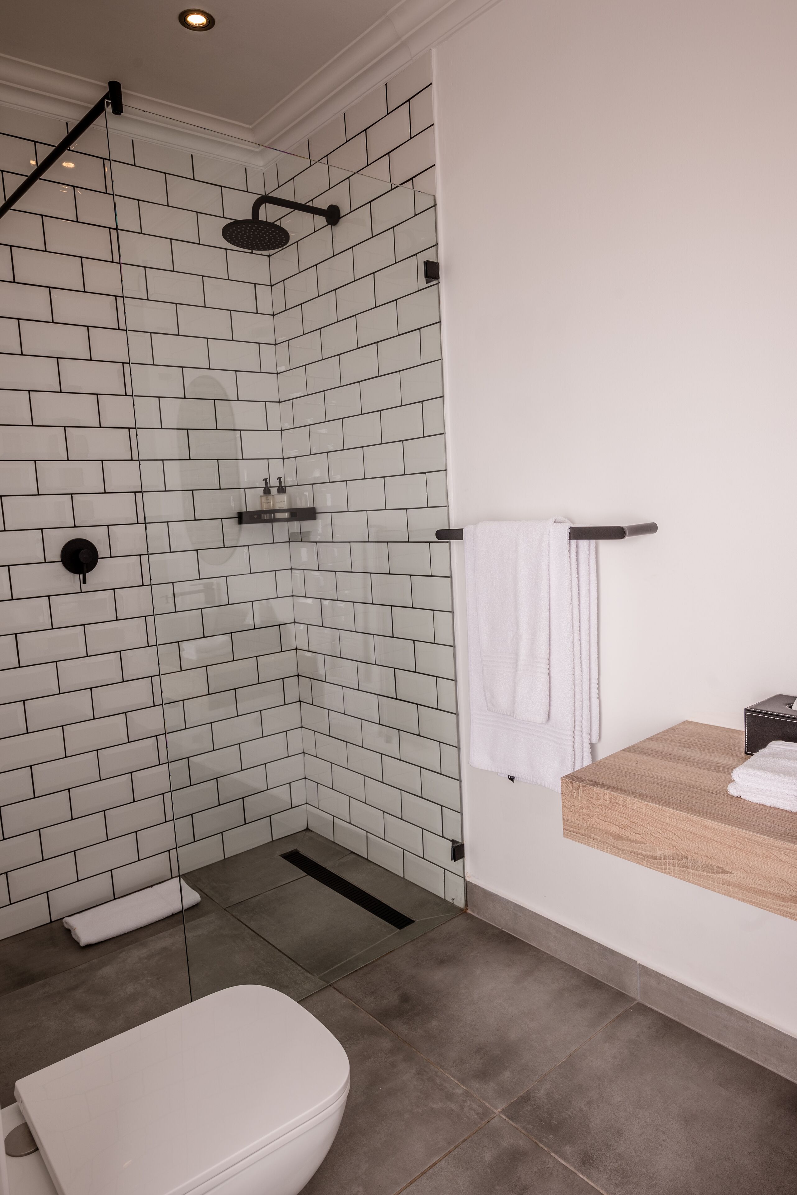 A modern bathroom with white subway tiles, a glass-enclosed shower, a white toilet, and a wooden vanity with a towel rack.
