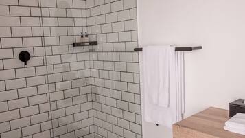 A modern bathroom with white subway tiles, a glass-enclosed shower, a white toilet, and a wooden vanity with a towel rack.