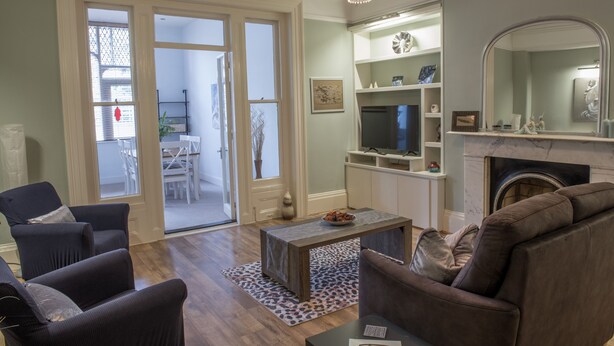 A living room with a fireplace, a television, and a dining area visible through glass doors. - Toothbrush Apts - Ipswich Fonnereau Road (Ipswich)