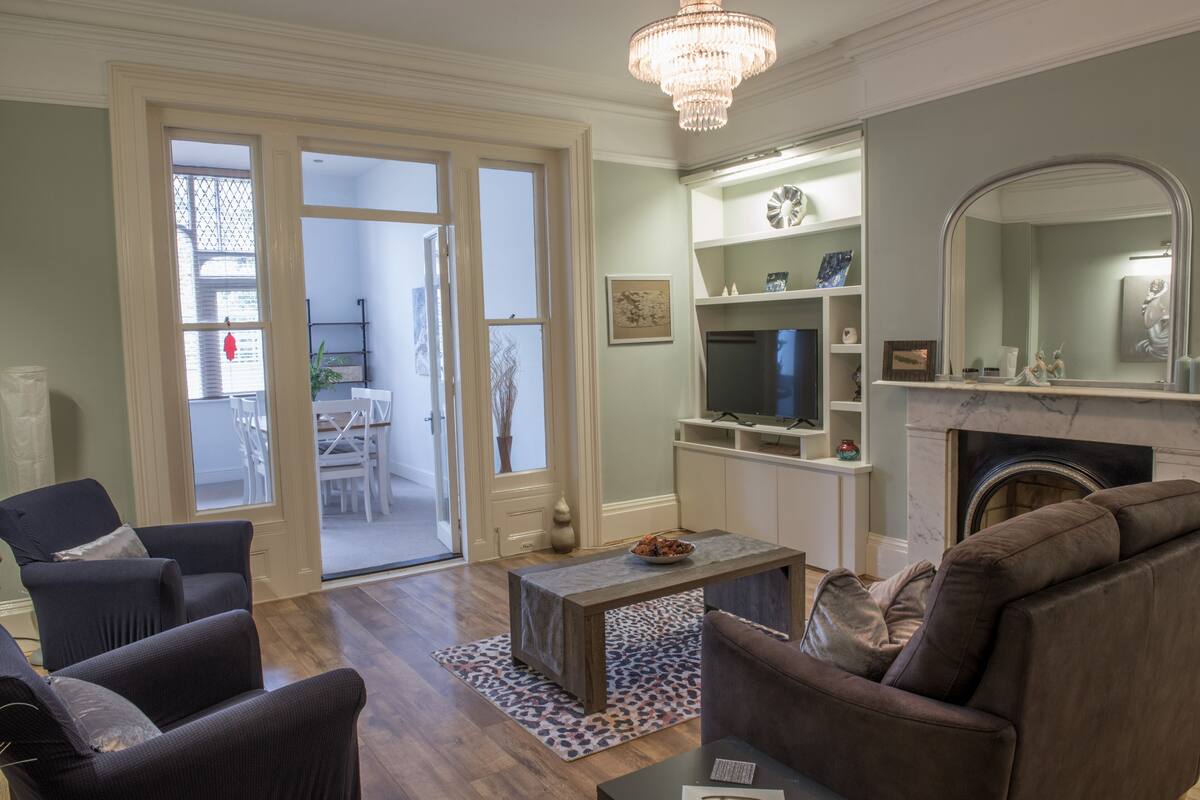 Sala de estar con chimenea, televisor y un comedor visible a través de puertas de vidrio.