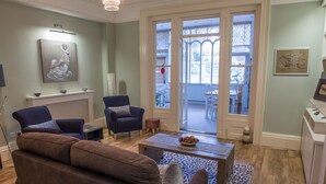 A living room with a brown sofa, two armchairs, a coffee table, and a fireplace. There is a door leading to a balcony with a view of the outside. - Toothbrush Apts - Ipswich Fonnereau Road (Ipswich)