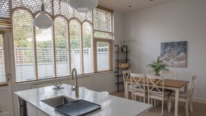 A modern kitchen with a central island, white cabinetry, and a large window with blinds. - Toothbrush Apts - Ipswich Fonnereau Road (Ipswich)