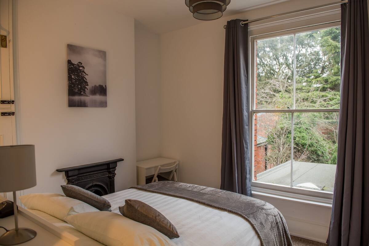 Un dormitorio con cama, chimenea, escritorio y ventana con cortinas.