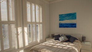 A bedroom with a bed, nightstands, a painting, and large windows with blinds. - Toothbrush Apts - Ipswich Fonnereau Road (Ipswich)
