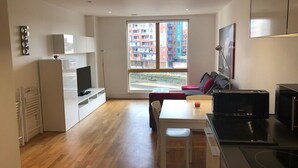 A modern apartment with a kitchen, dining area, and a large window offering a city view. - Toothbrush Apartments - Ipswich Quayside (Ipswich)