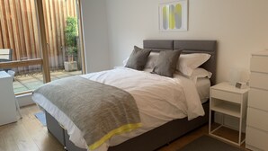 A modern bedroom with a large bed, a bedside table, and a view of the outdoors. - Toothbrush Apartments - Ipswich Quayside (Ipswich)
