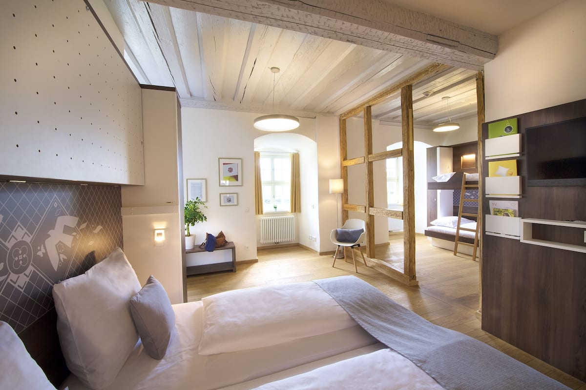 A modern hotel room with a large bed, a desk, and a view of the adjacent room.