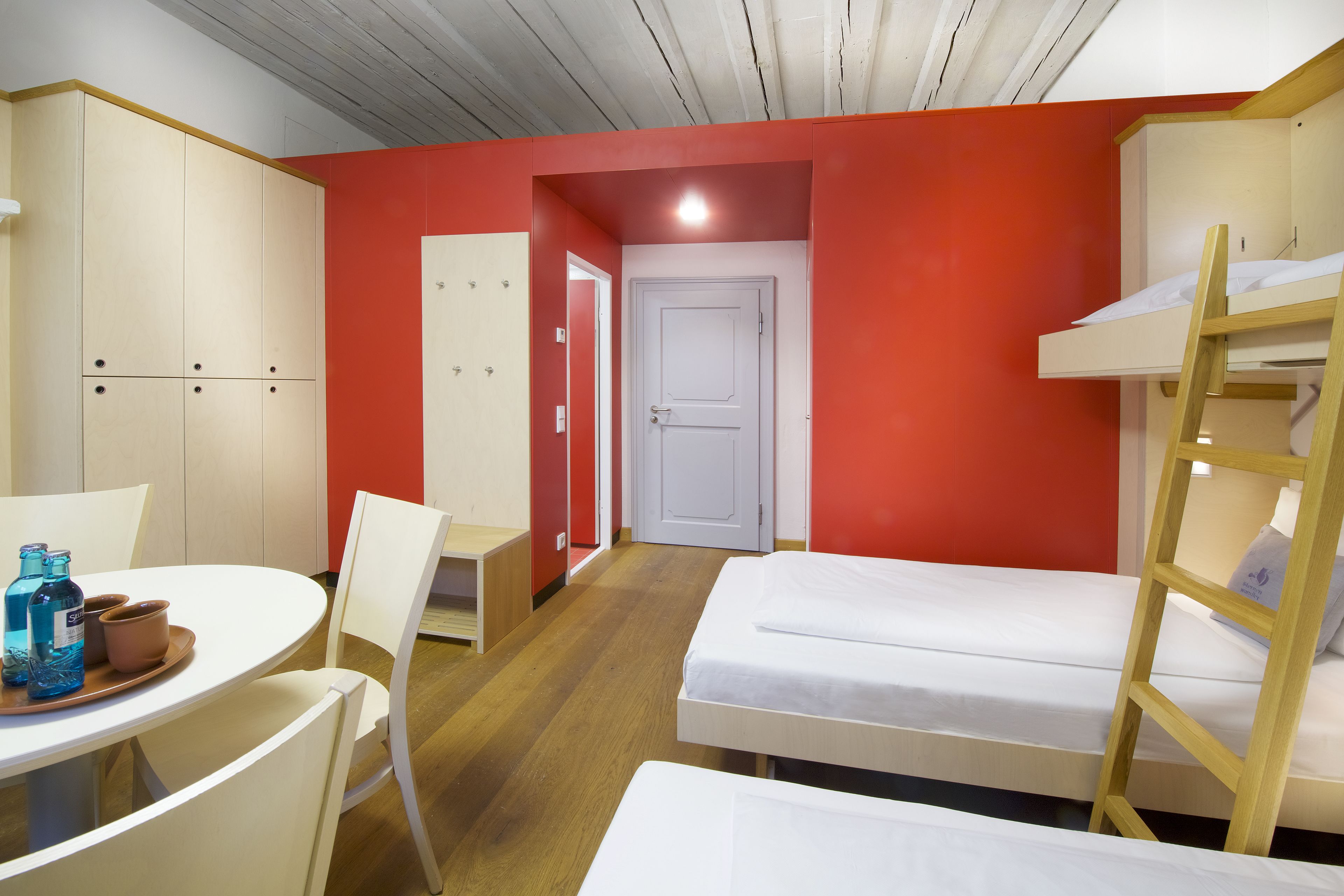 Ein Zimmer mit Etagenbetten, einem Schreibtisch mit Stühlen und einem Tisch mit Flaschen.