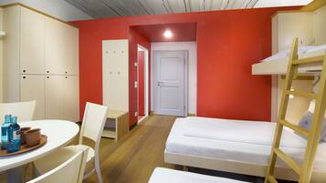 Ein Zimmer mit Etagenbetten, einem Schreibtisch mit Stühlen und einem Tisch mit Flaschen.