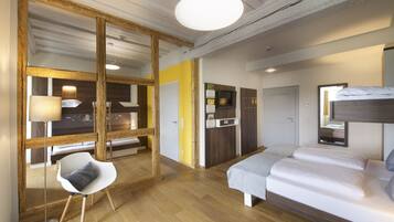 A modern hotel room with a wooden floor, a bed, a desk with a chair, a mirror, and a large window.