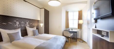 Habitación de hotel con dos camas, un escritorio, una silla, un televisor y una ventana con cortinas.