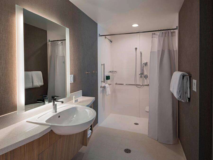 A modern bathroom with a large mirror, two sinks, a shower, and a toilet.