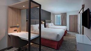 Een hotelkamer met twee bedden, een bureau, een stoel, een televisie en een groot raam.