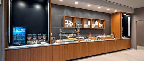 A modern breakfast bar with a self-service beverage dispenser, a variety of food items, and a display of decorative items.