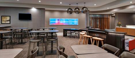 A modern hotel lobby with multiple seating areas, a reception desk, and a large digital display.