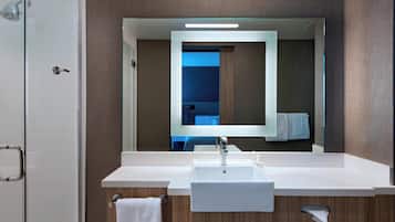 A modern bathroom with a large mirror, a white sink, and a shower area.