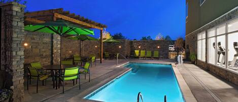 A pool area with a stone wall, green chairs, and umbrellas.