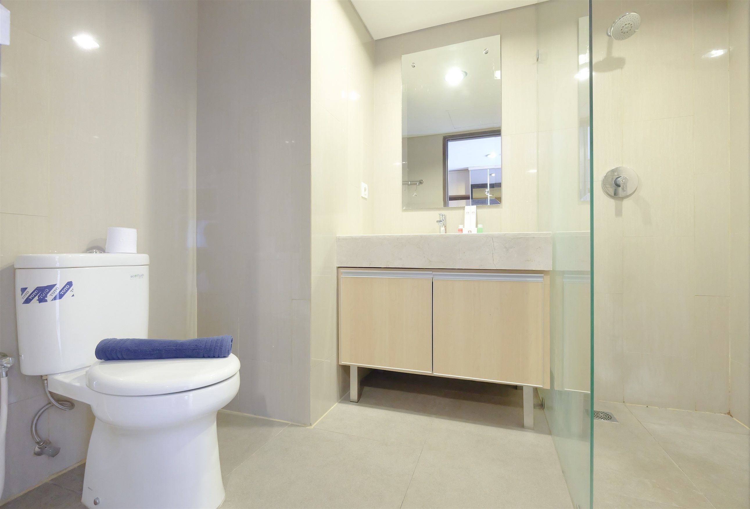 Un baño moderno con inodoro, cabina de ducha de vidrio y tocador color beige con espejo.