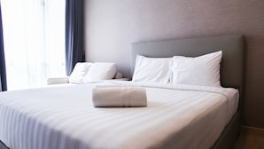 A neatly made bed with white linens and pillows, a grey headboard, and a rolled white towel on the bed. - Brand New Studio @ Menteng Park Apartment (Jakarta)