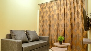 A room with a grey sofa, a small round table with a potted plant, and a curtain with a patterned design. - Big 2 BR (76 sqm) Apartment Grand Palace/Pallazo Kemayoran (Jakarta)