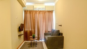 A small living area with a sofa, a small table with a plant, a TV on a shelf, and a curtain. - Best of the Best 3BR Apartment Grand Palace/Pallazo Kemayoran (Jakarta)