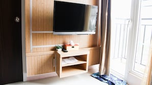 A room with a mounted TV, a small wooden cabinet with a tissue box and remote, and a sliding glass door to a balcony. - Best Price 2BR Mutiara Bekasi Apartment (Bekasi)