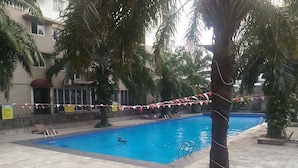 A swimming pool area with tiled flooring, palm trees, and a building in the background. - Best Price 2BR Mutiara Bekasi Apartment (Bekasi)