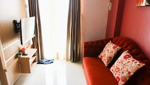 A compact living space with a red sofa, a mounted TV, and a wooden cabinet with a small plant. - Best Price 2BR Mutiara Bekasi Apartment (Bekasi)