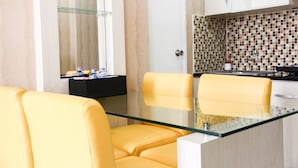A modern dining area with a glass table and yellow chairs, a kitchen with a tiled backsplash, and a white cabinet. - Pool View 2BR Mutiara Bekasi Apartment (Bekasi)