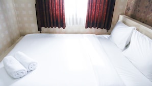 A neatly made bed with white linens and two rolled towels, a wooden headboard, and a window with red curtains. - Pool View 2BR Mutiara Bekasi Apartment (Bekasi)