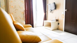 A modern living room with a sofa, a flat-screen TV mounted on the wall, and a small side table. - Pool View 2BR Mutiara Bekasi Apartment (Bekasi)