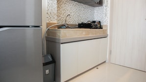 A compact kitchen with a refrigerator, a sink, and a microwave. - Cozy Studio Apartment at Elpis Residence (Jakarta)