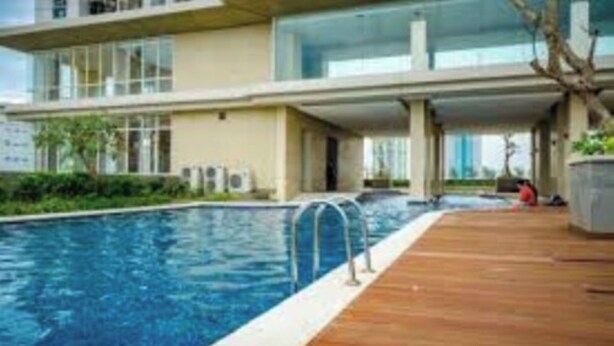 A modern building with a swimming pool and wooden deck. - Cozy Studio Apartment at Elpis Residence (Jakarta)