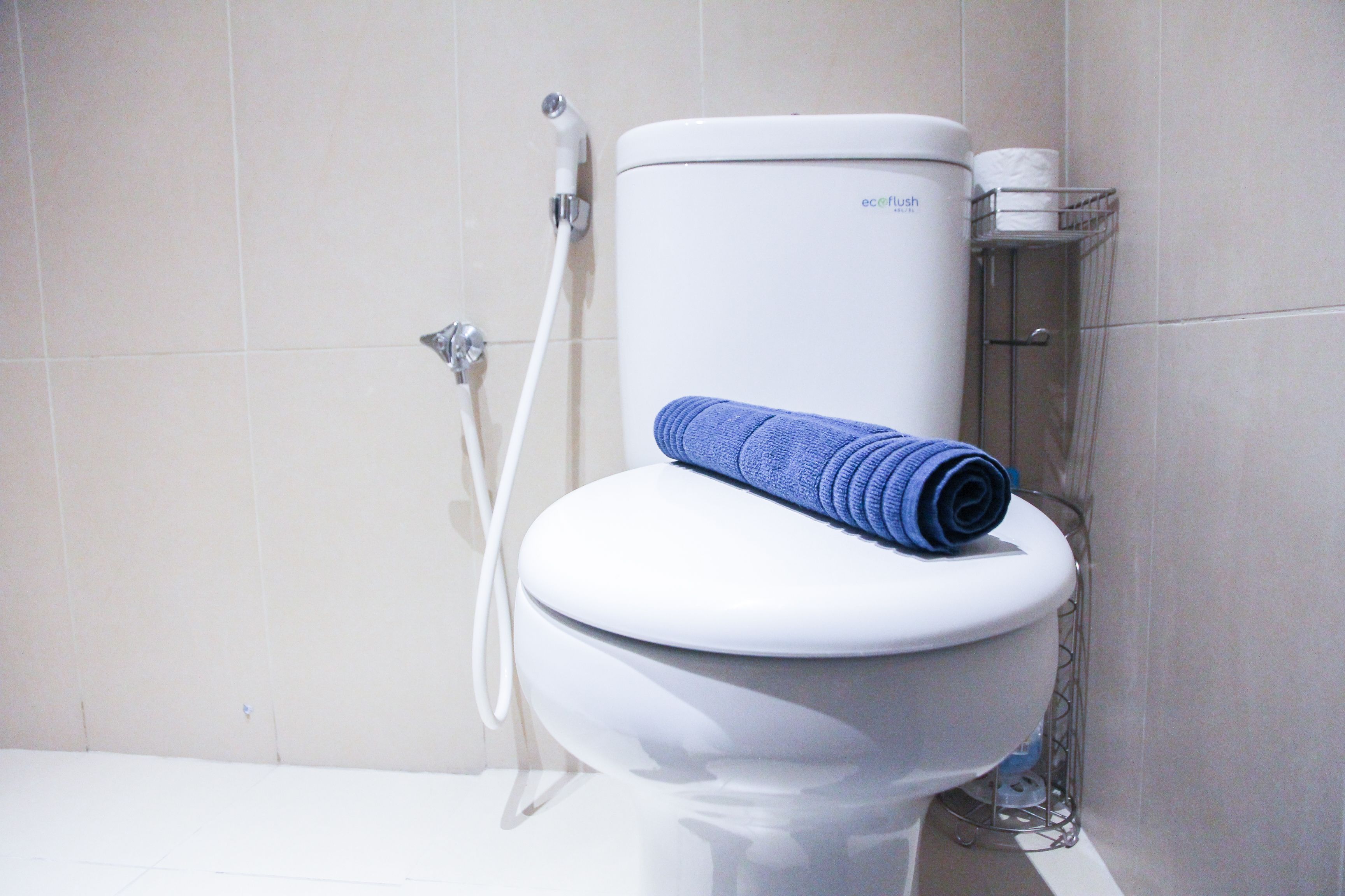 Des toilettes blanches avec une serviette bleue posée sur le couvercle et un porte-rouleau de papier toilette sur la droite.