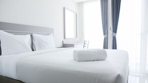 A neatly made bed with white linens and pillows, a bedside table with a lamp, and a large window with curtains. - Cozy Studio Apartment at Elpis Residence (Jakarta)