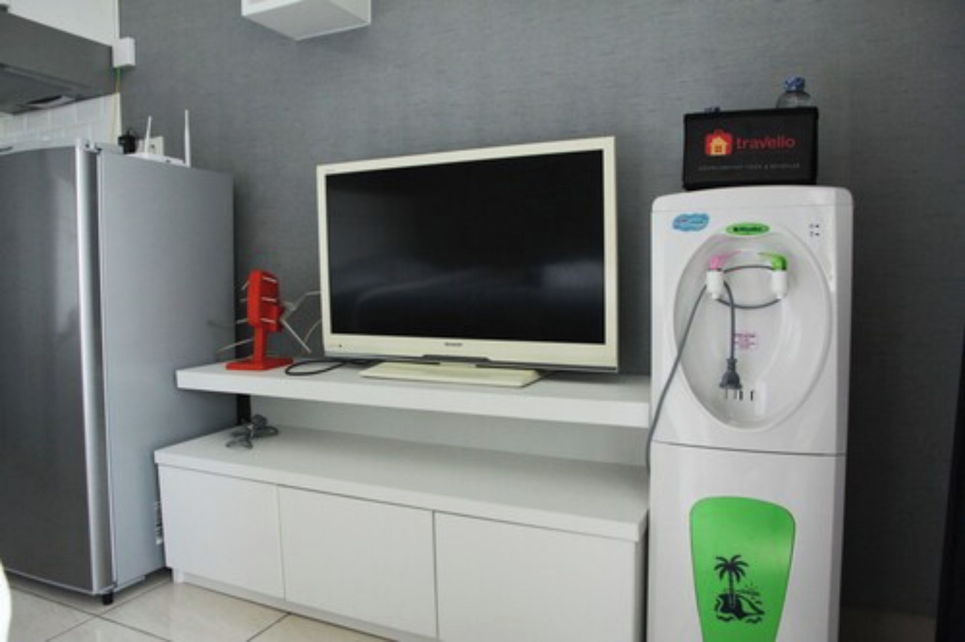 A modern kitchen with a refrigerator, a flat-screen TV, and a water dispenser.