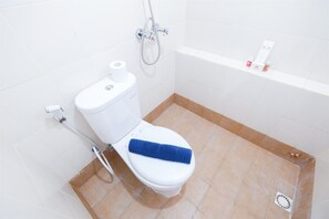 Een badkamer met een wit toilet, een blauwe handdoek op de zitting, een douchekop en een klein plankje met toiletartikelen.