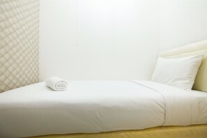 A neatly made bed with a rolled white towel, a cream-colored headboard, and a plain wall.