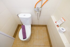 A bathroom with a toilet, a shower head, and a roll of toilet paper on the wall.