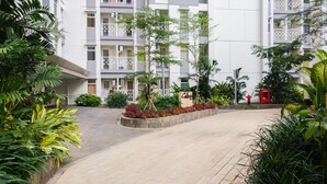 A modern building with multiple balconies, surrounded by lush greenery and a paved walkway. - 2BR + Sofa Bed The Springlake Summarecon Bekasi Apartment (Bekasi)