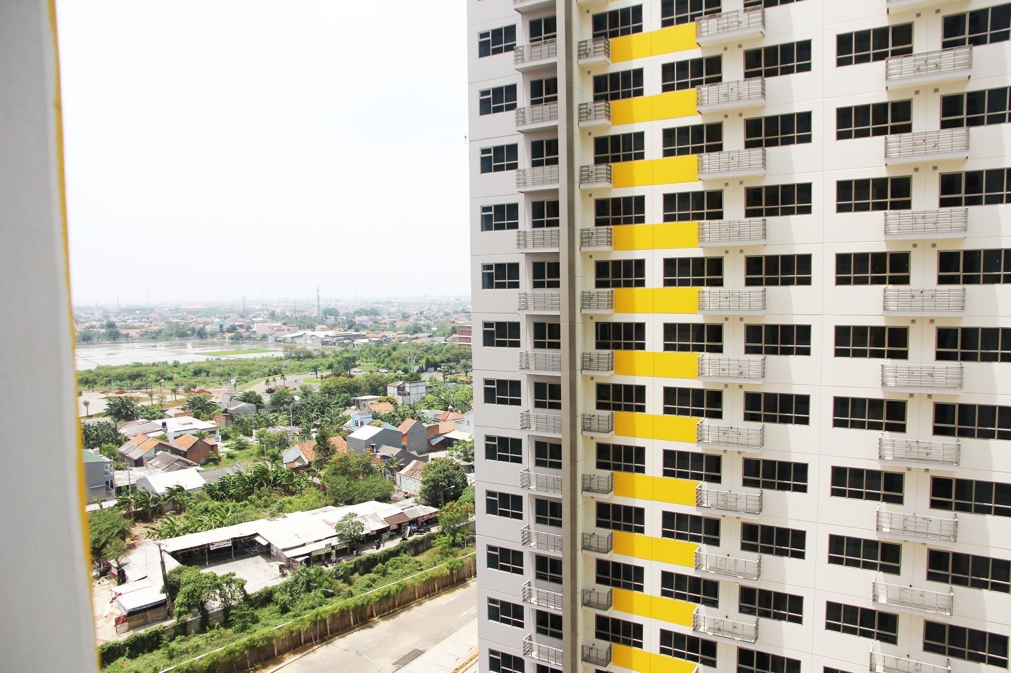 A high-rise building with multiple balconies, a view of a river and surrounding residential area.