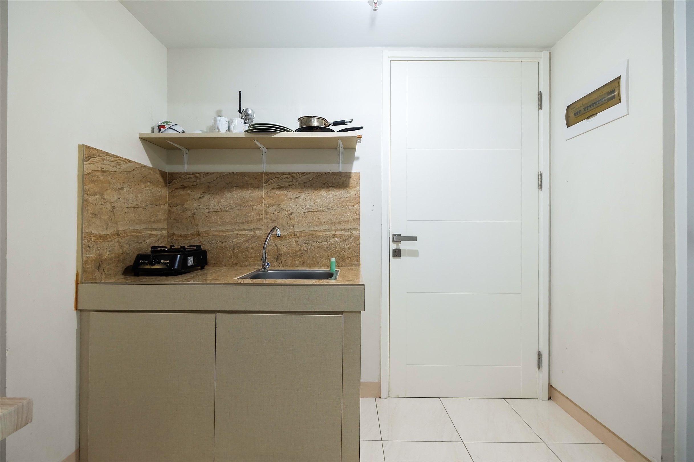A compact kitchen with a built-in sink, a countertop, and a small shelf above.