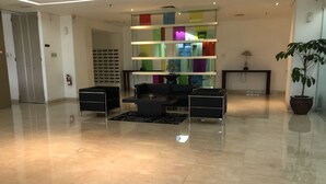 A modern lobby with a glass partition, a black sofa, a coffee table, and a potted plant.
