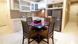A modern kitchen with white cabinets, a stainless steel refrigerator, and a dining table with four chairs.
